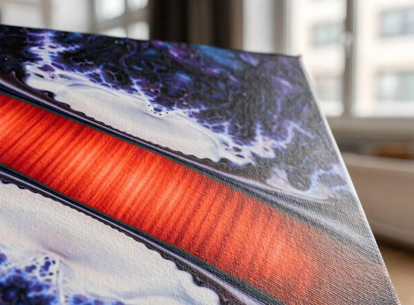Close-up of a canvas print of bold abstract art, with a vivid red stripe across swirling purple, blue, and white, showing the canvas texture and wrapped edge